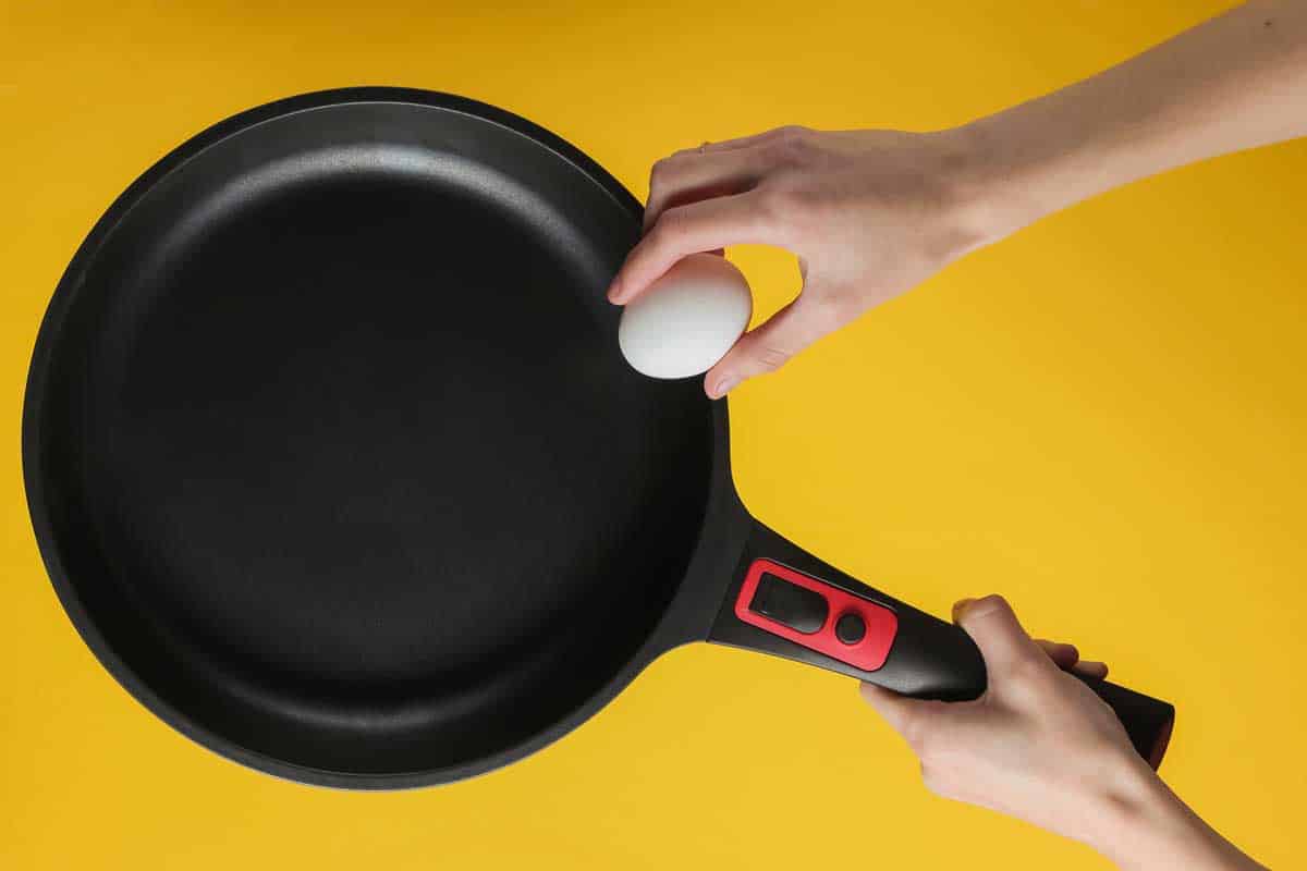 Female hand spits chicken egg on a frying pan with non-stick coating.