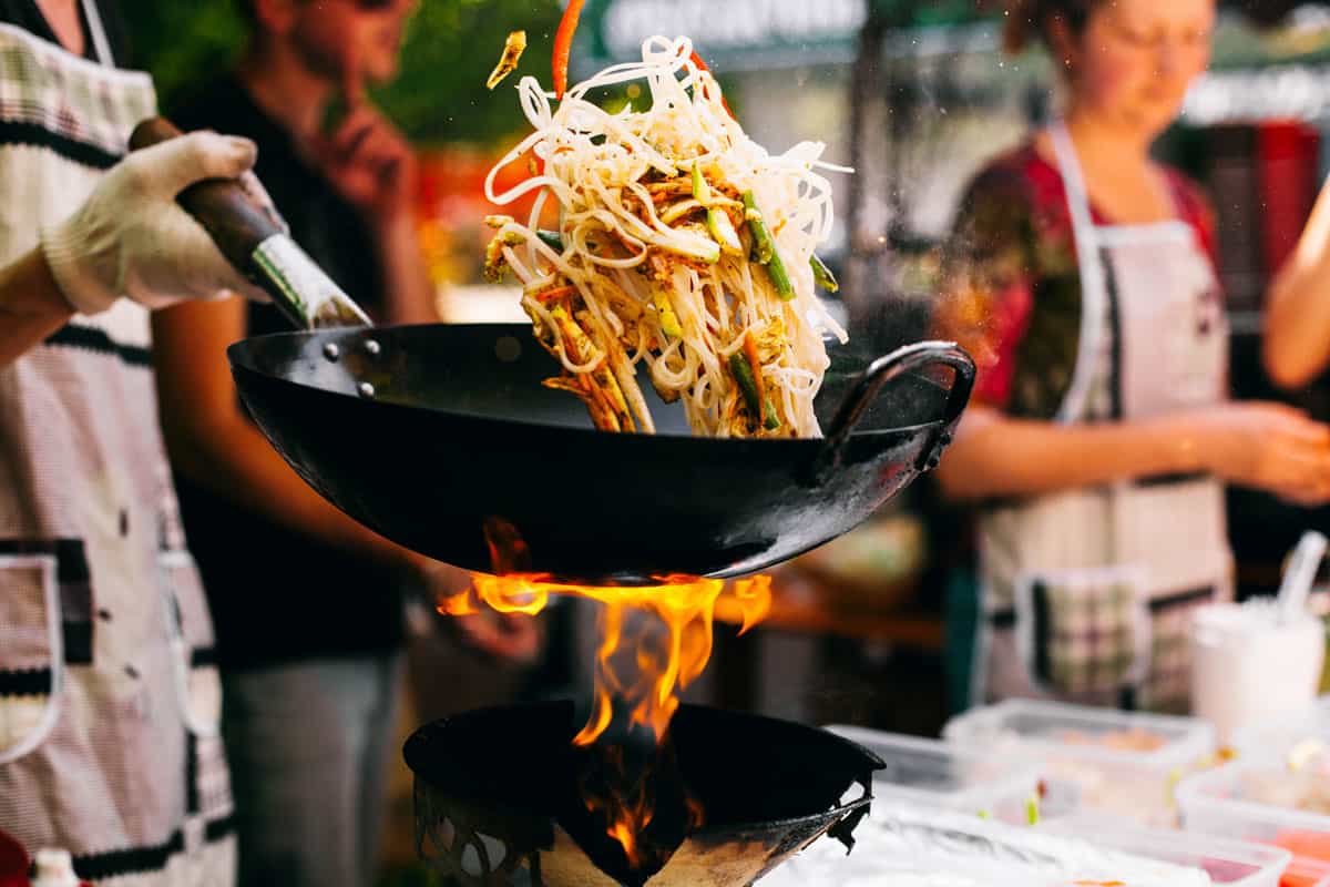 A cook cooking ramen in a wok with all other sorts of vegetables mixed together