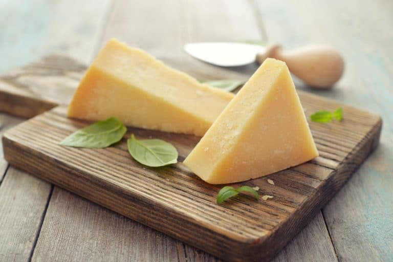 Parmesan cheese layed on chopping board for slicing with greens on the side, How to Grate Parmesan Cheese Without a Grater [5 Options Revealed]