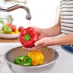 Woman washing huge red bell pepper in preparation for cooking, 11 Types Of Kitchen Strainers [Inc. Colanders And Sieves]