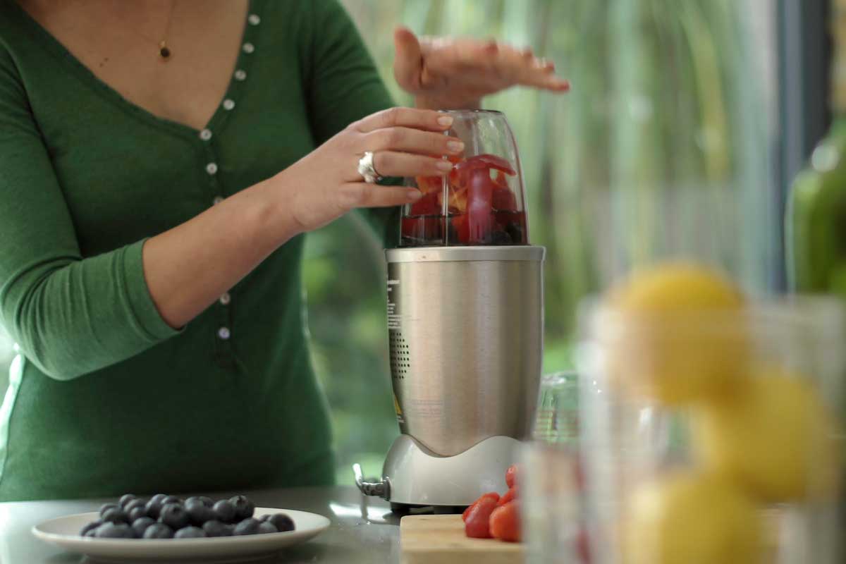A young woman making a fruit smoothie drink using a nutibullet after loading it with fruit.