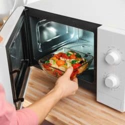 Woman putting bowl with vegetables in microwave oven, closeup