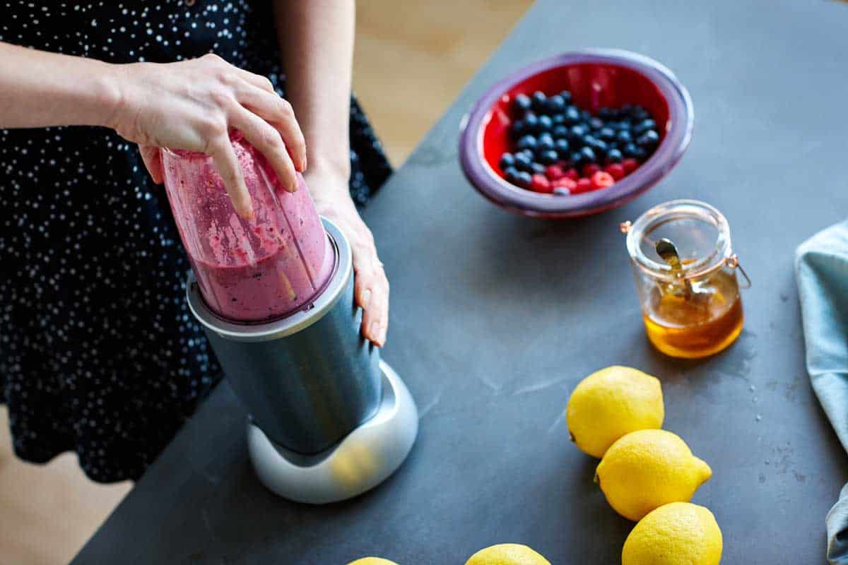 Close up of woman making fruit juice using nutribullet at home in kitchen