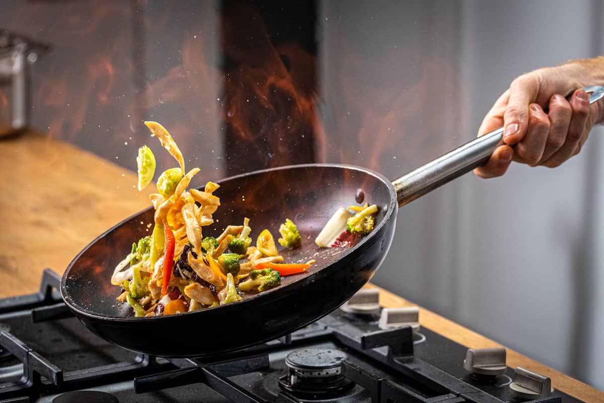 A man cooking a mix of veggies on his stir fry wok