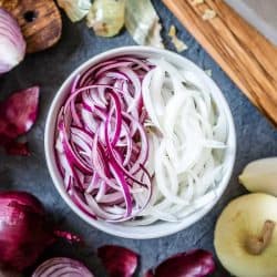 Top view of a bowl full of red and golden sliced onions with a wooden cutting board on the side, What’s The Best Way To Store A Cut Onion?
