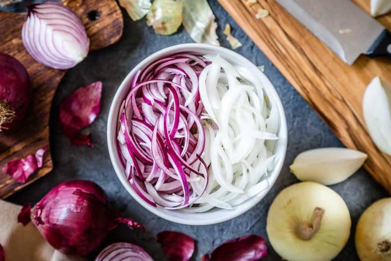Top view of a bowl full of red and golden sliced onions with a wooden cutting board on the side, What’s The Best Way To Store A Cut Onion?