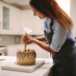A woman making a fondant cake and putting on frosting using a piping bag, How To Store A Fondant Cake? [5 Easy Solutions]