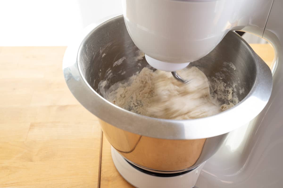 A stand mixer mixing bread dough on a stainless steel mixing bowl
