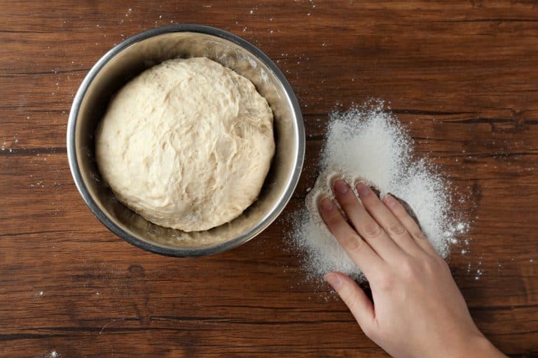 A woman spreading flour on a wooden table before mixing her raw bread dough, Can You Safely Mix Bread Dough in a Stainless Steel Bowl?