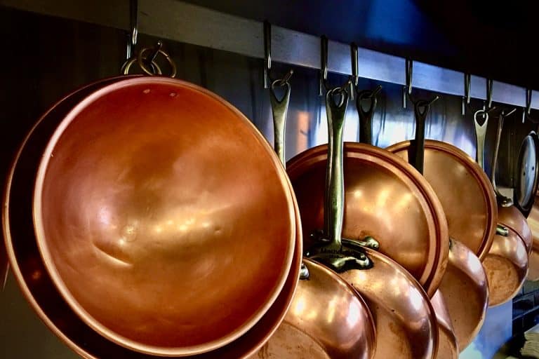 Clean copper sauce pans and mixing bowls hanged on a restaurant wall, How To Clean A Copper Mixing Bowl [4 Effective Ways]