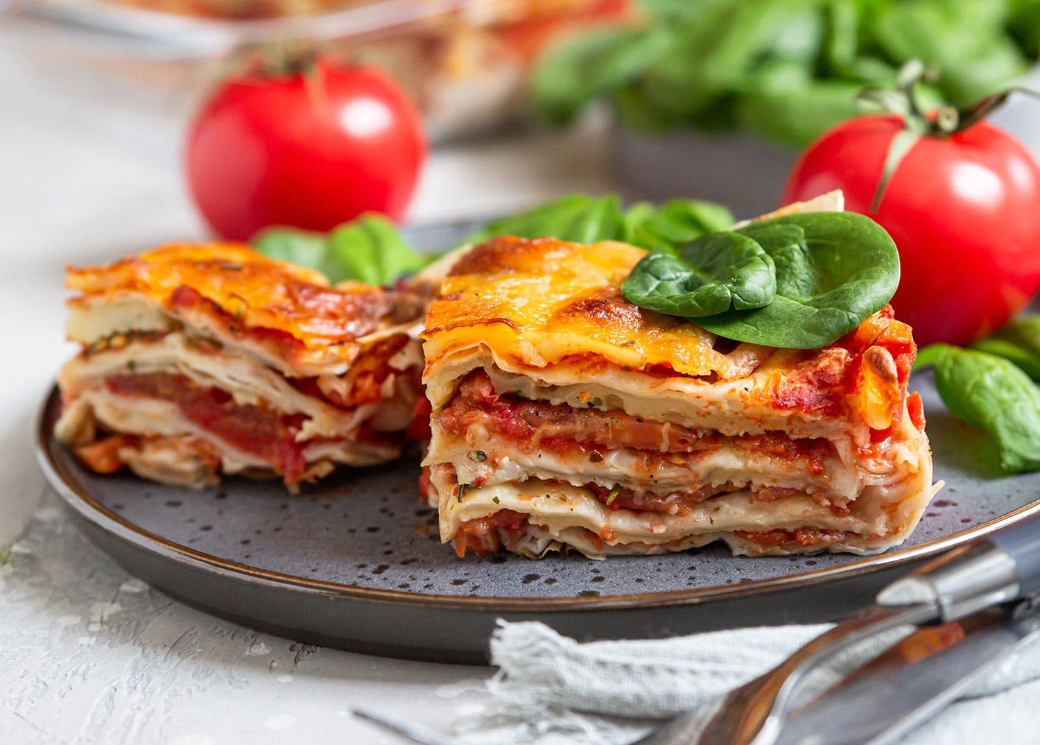 Italian lasagna with tomato sauce and cheese served with tomatoes and spinach