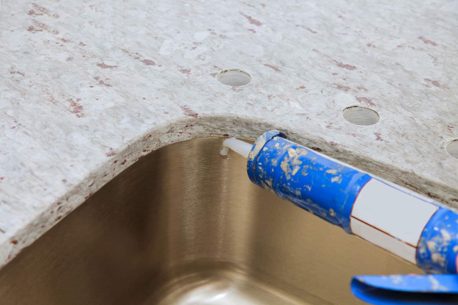 Gun putting silicone sealant to installing a kitchen sink with modern decorative granite countertops