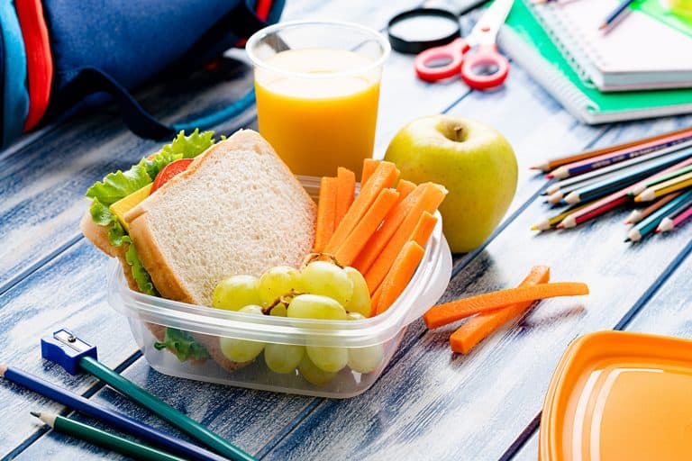 Healthy food for kids concepts: well balanced school lunch box shot on blue table. School supplies are around the lunch box, How To Seal Plastic Food Containers [4 Cool Tricks!]