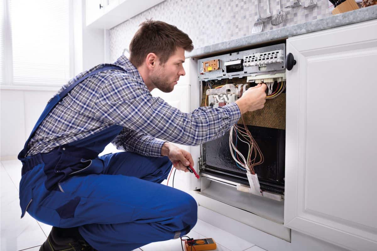 Male technician checking dishwasher with digital multimeter in kitchen