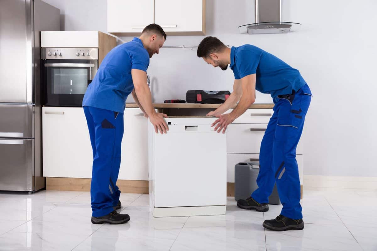 Male movers in uniform placing dishwasher in kitchen