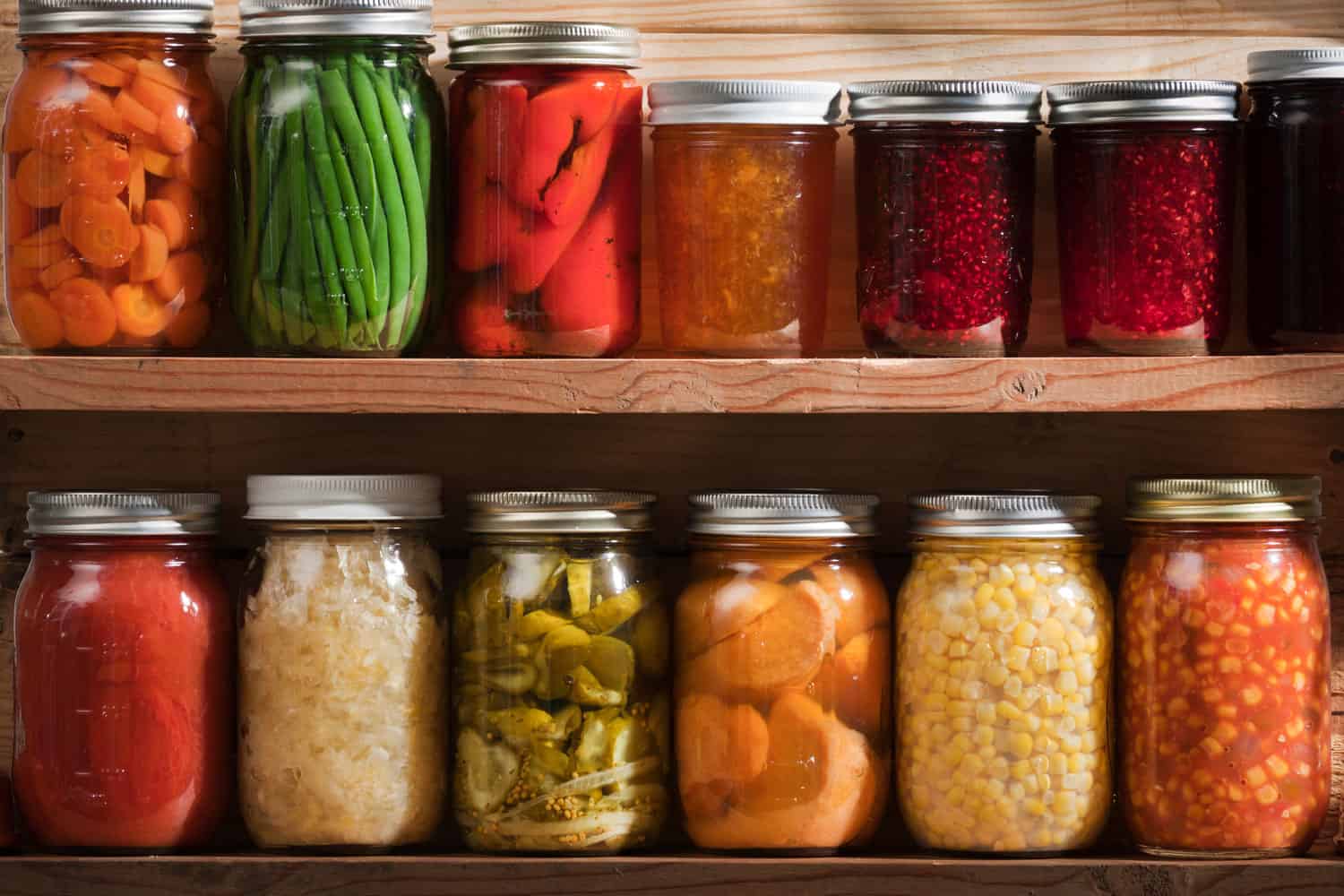 Two wooden shelves holding a variety of canned vegetables and fruits, lined up in rows of glass jars