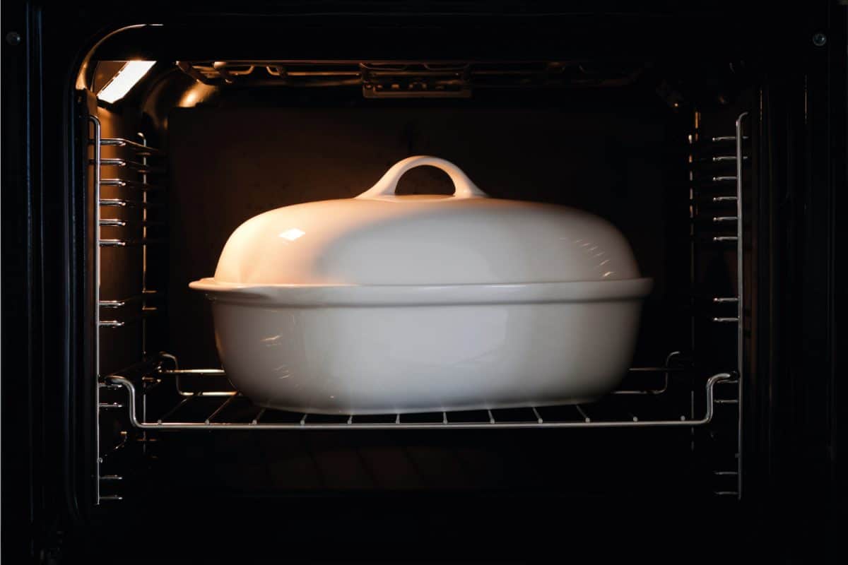 White porcelain baking dish with lid inside of dark oven with light on