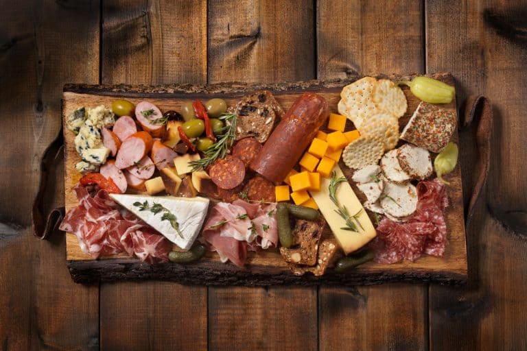 A charcuterie board with lots of different delicacies on it placed on a scorched wooden table, What Kind of Wood is Used for Cheese and Charcuterie Board?