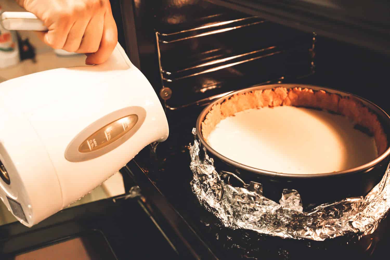 Pouring water bath for cheesecake inside the oven
