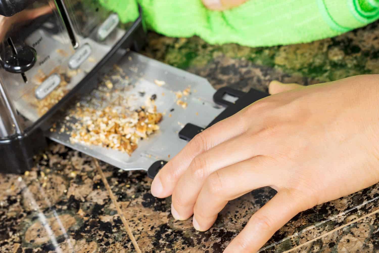 A woman removing the bread crumb tray of a toaster