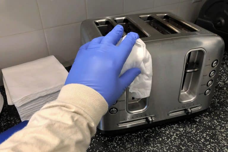 Woman wearing gloves cleaning toaster oven in the kitchen, How To Clean A Toaster [6 Steps]