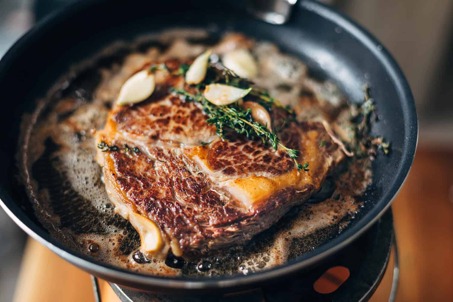 Ribeye steak with butter, thyme, and garlic on hot cast iron pan