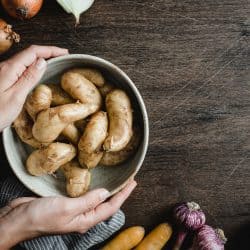 Point of view of a female holding a bowl full of fresh potatoes with onions and carrots on wooden table in kitchen, What Potatoes Are Best For Stews And Soups? [6 Excellent Options]