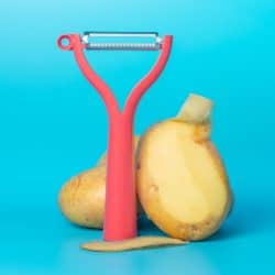 Two potatoes with a peeler on a blue background, 8 Types of Potato Peelers