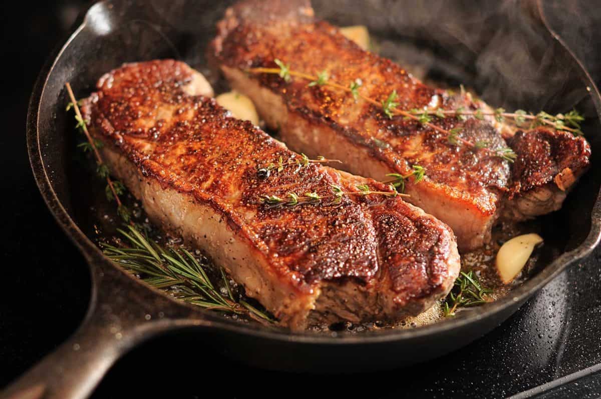 Two strip loins pan seared in a cast iron pan with herbs and garlic