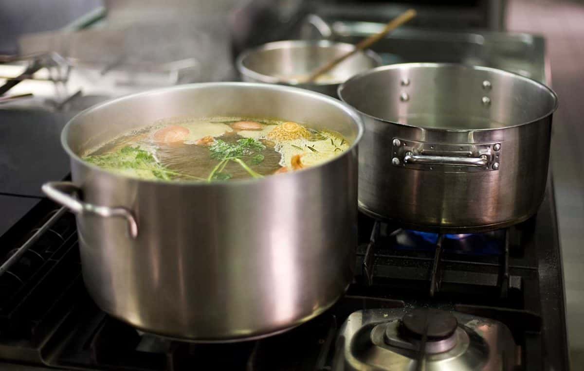 Vegetable broth is simmering on a gas stove in a commercial kitchen