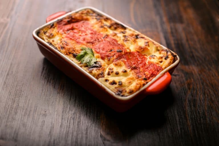 A freshly baked pot of lasagna on a red ceramic container, How Long Do You Let a Lasagna Sit?
