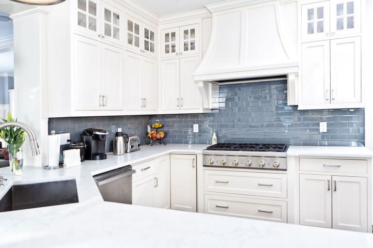 A gorgeous white themed kitchen with white paneled cabinetry, blue tiled backsplash, and a white kitchen countertop, How To Eliminate The Gap Between Range And Countertop
