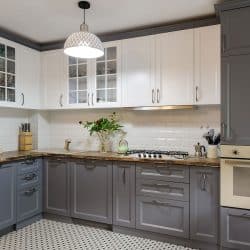 A modern gray themed kitchen area with gray cabinets, white paneled upper cabinets, and a white tiled backsplash, 5 Ways To Waterproof Cabinets Under The Kitchen Sink