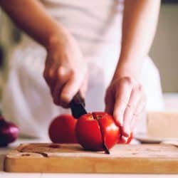 A woman slicing a piece of tomato on her chopping board, How To Properly Dice A Tomato [3 Ways]
