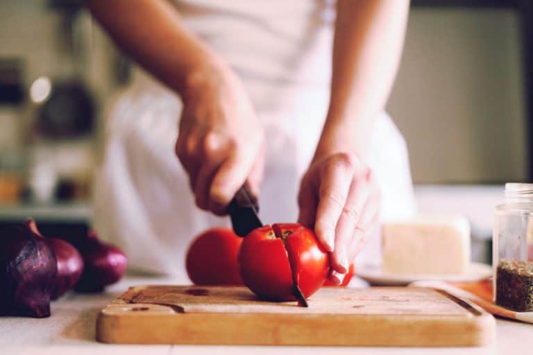 A woman slicing a piece of tomato on her chopping board, How To Properly Dice A Tomato [3 Ways]