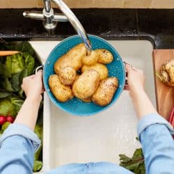 A woman washing fresh potatoes on a washing tray on her sink, Should You Wash Potatoes Before Or After Peeling?
