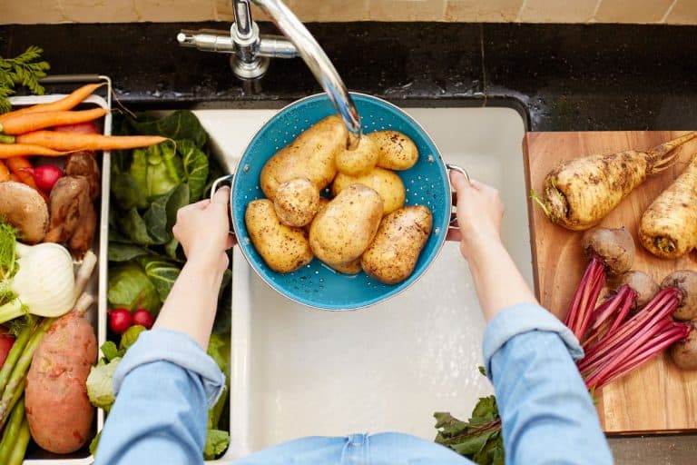 A woman washing fresh potatoes on a washing tray on her sink, Should You Wash Potatoes Before Or After Peeling?
