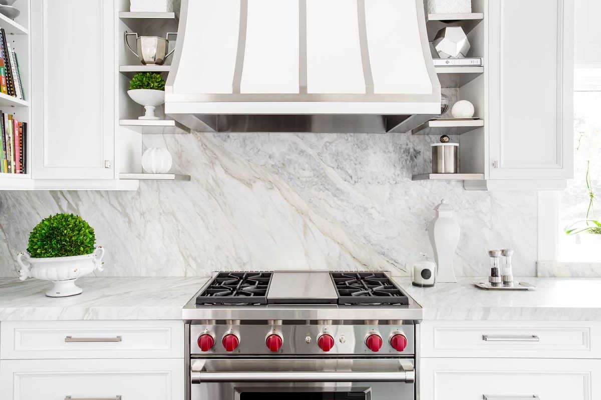 Bright horizontal image of classic white kitchen, with gas range and marble backsplash