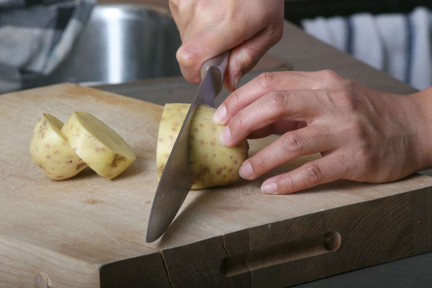 One person slicing a potatoes on a cutting board
