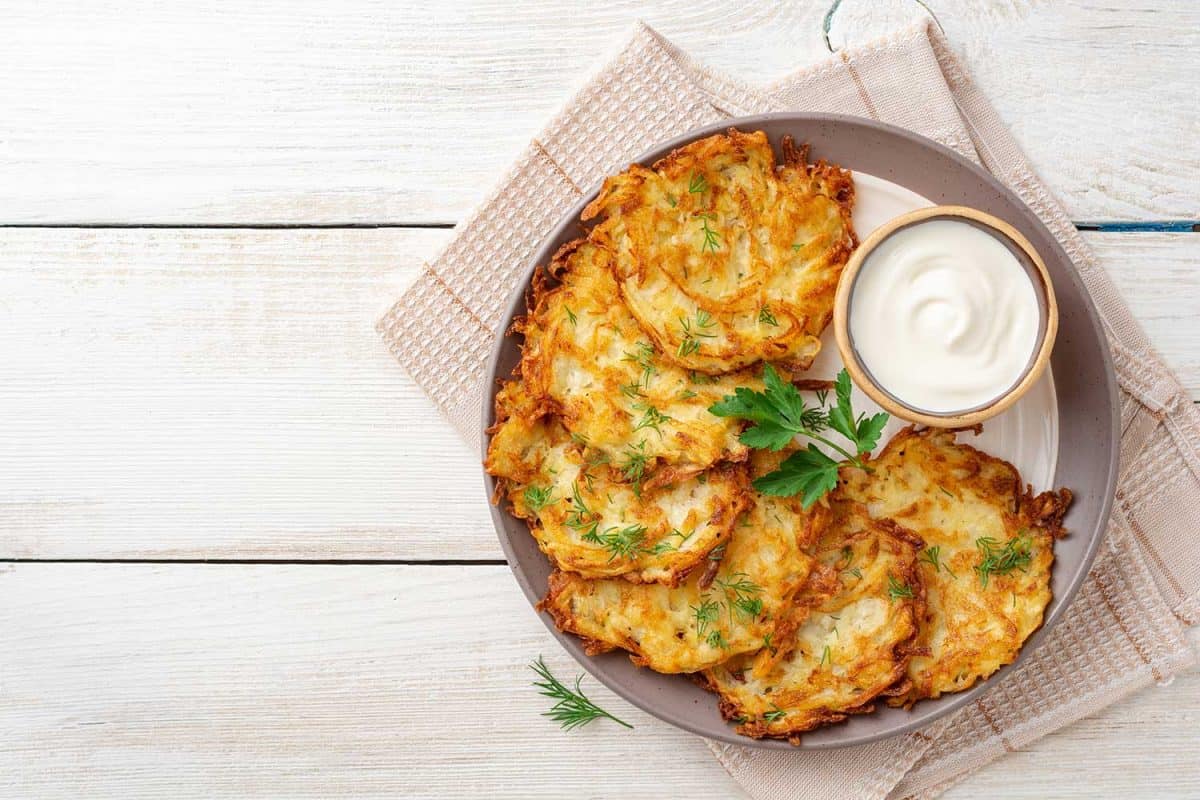 Potato pancakes with sour cream in plate on white wooden table