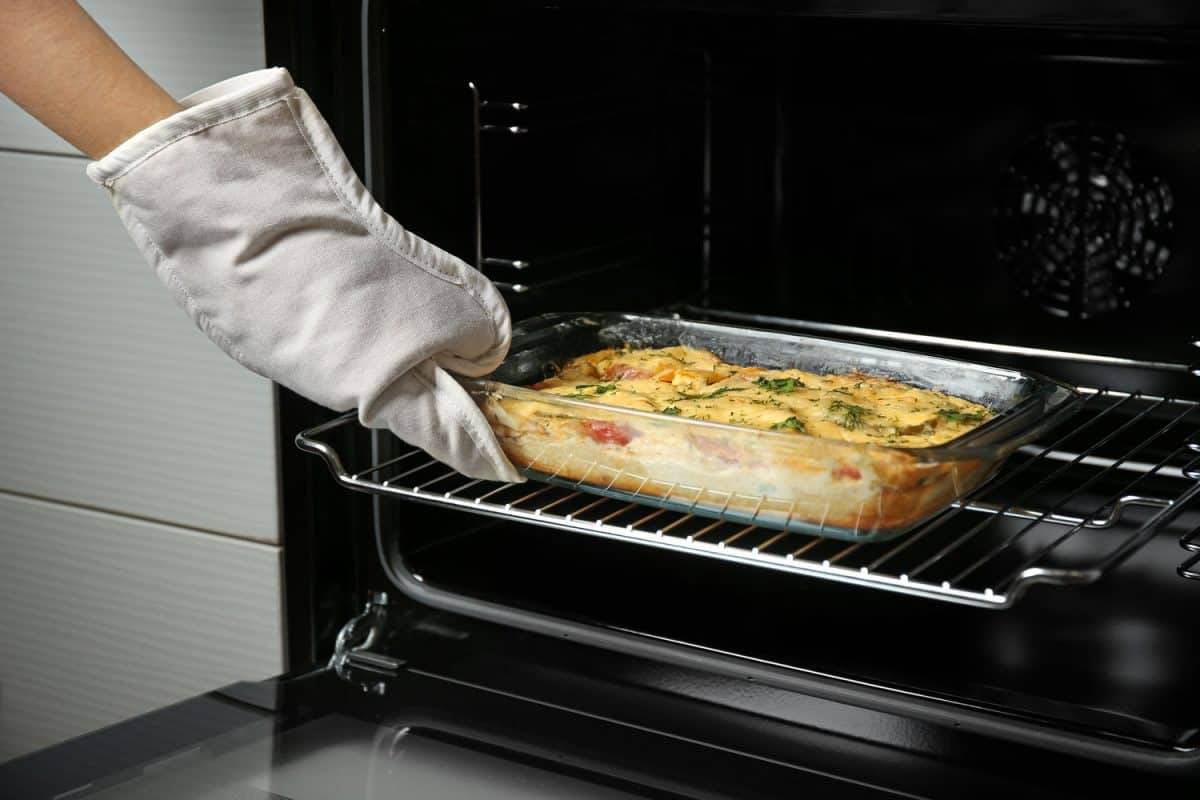 A woman taking a freshly baked lasagna off the oven
