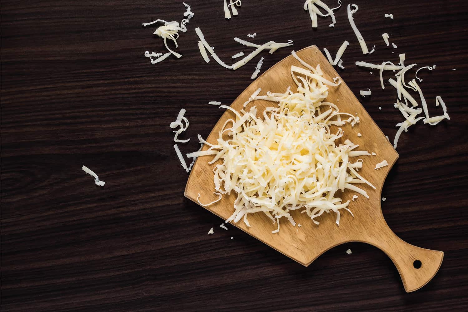 Grated cheese for cooking on a cutting board on a dark background