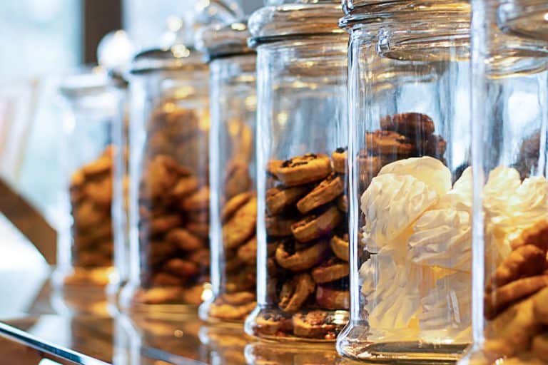 Huge cookie jars lined up at a bar table of a coffee shop, How To Make A Cookie Jar Airtight [The Key To Keeping Cookies Fresh!]