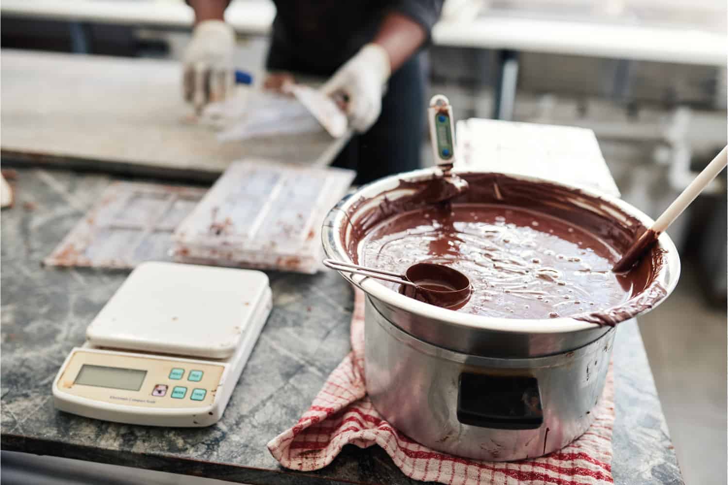 Melted chocolate in a bain marie on a table in an artisanal chocolate making factory being mixed and temperature monitored