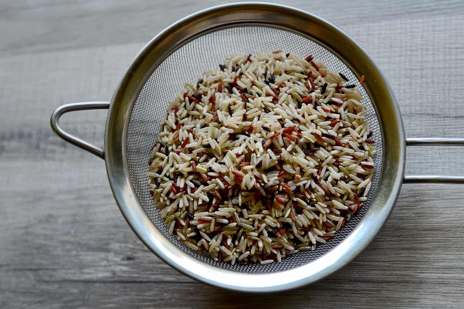 Mixture of long unpolished white and brown rice in a metallic strainer