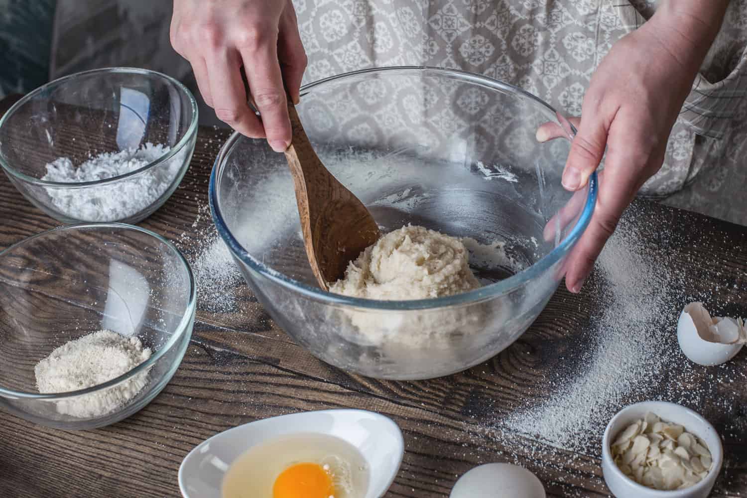 Woman stirring dough with spatula. Eggs, sugar, almond near on the table, What Size Mixing Bowl For Making Bread?