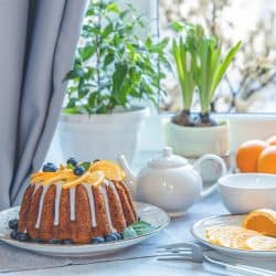 A delicious bundt cake topped with oranges and blue berries, How Long Should A Bundt Cake Cool In Pan Before Icing Or Cutting?