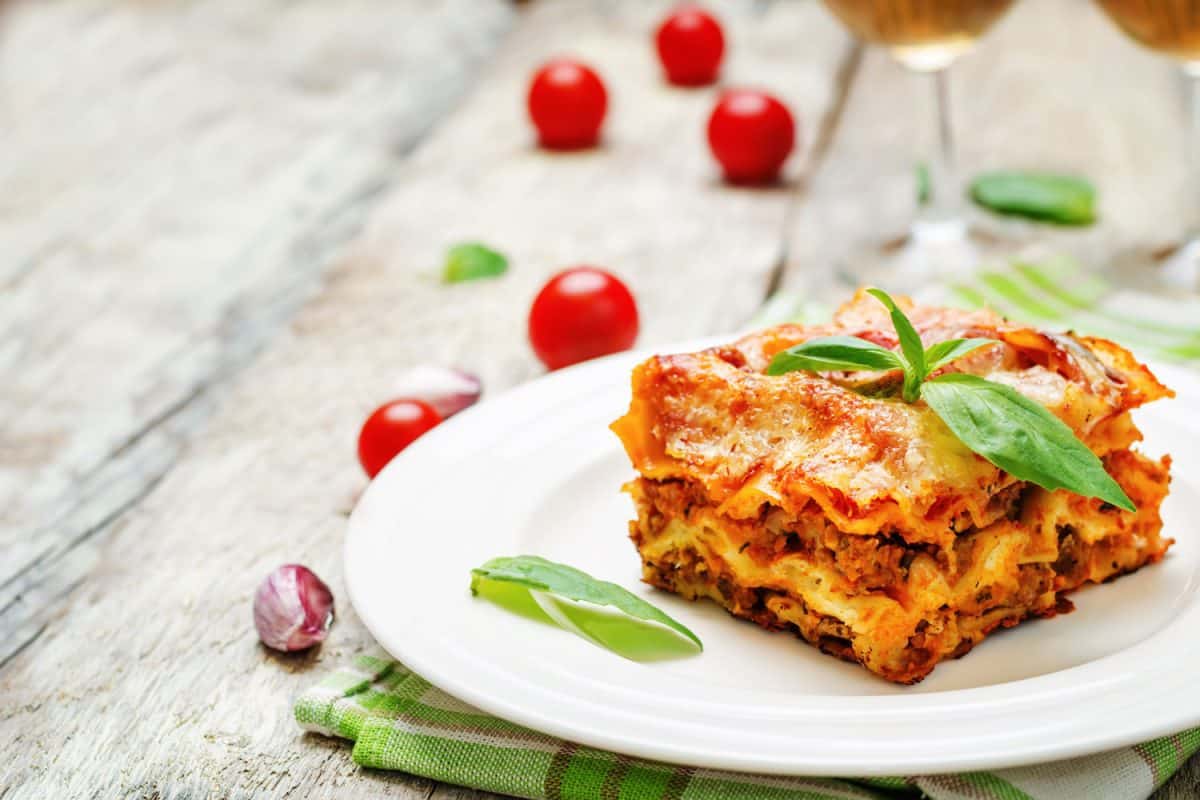 A delicious slice of lasagna on a white plate and other small tomatoes on the sides