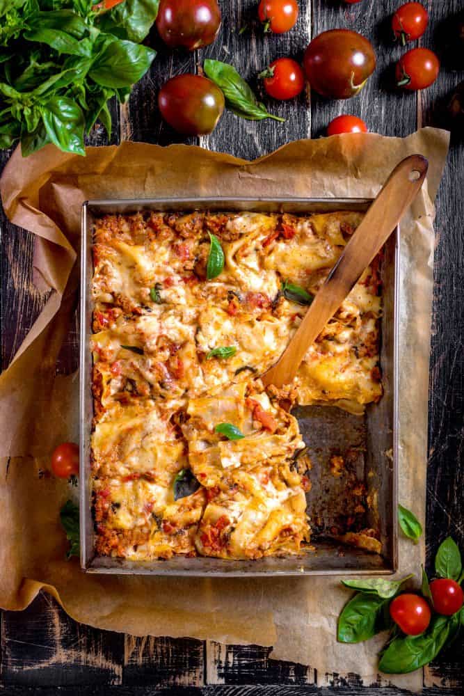 A freshly baked lasagna on a baking tray with a wooden spatula for serving