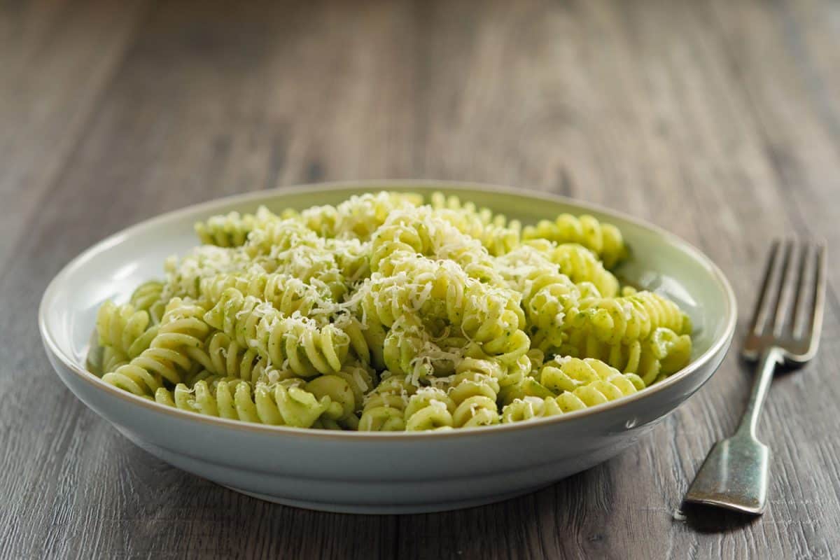A healthy version of pasta mixed with pesto sauce garnished with parmesan cheese